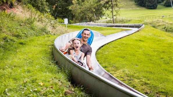 Ein Mann und ein Kind nutzen die Sommerrodelbahn am Freizeitzentrum Peterberg